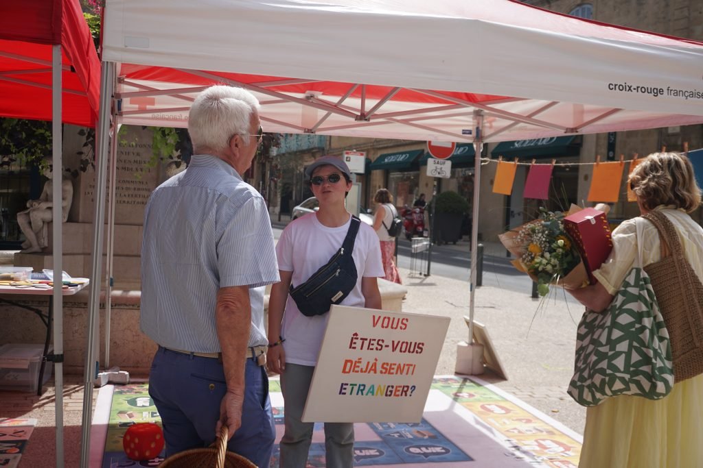 A caravaner holding a placard that reads "Have you ever felt like a foreigner?" and engaging in a conversation with a passerby. 